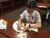 A girl is writing her favourite poem on the fan intently.