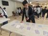 A student concentrates while flipping cards to solve a puzzle challenge, with classmates waiting their turn in the background.