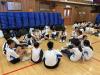 Students sit in a circle on the hall floor.